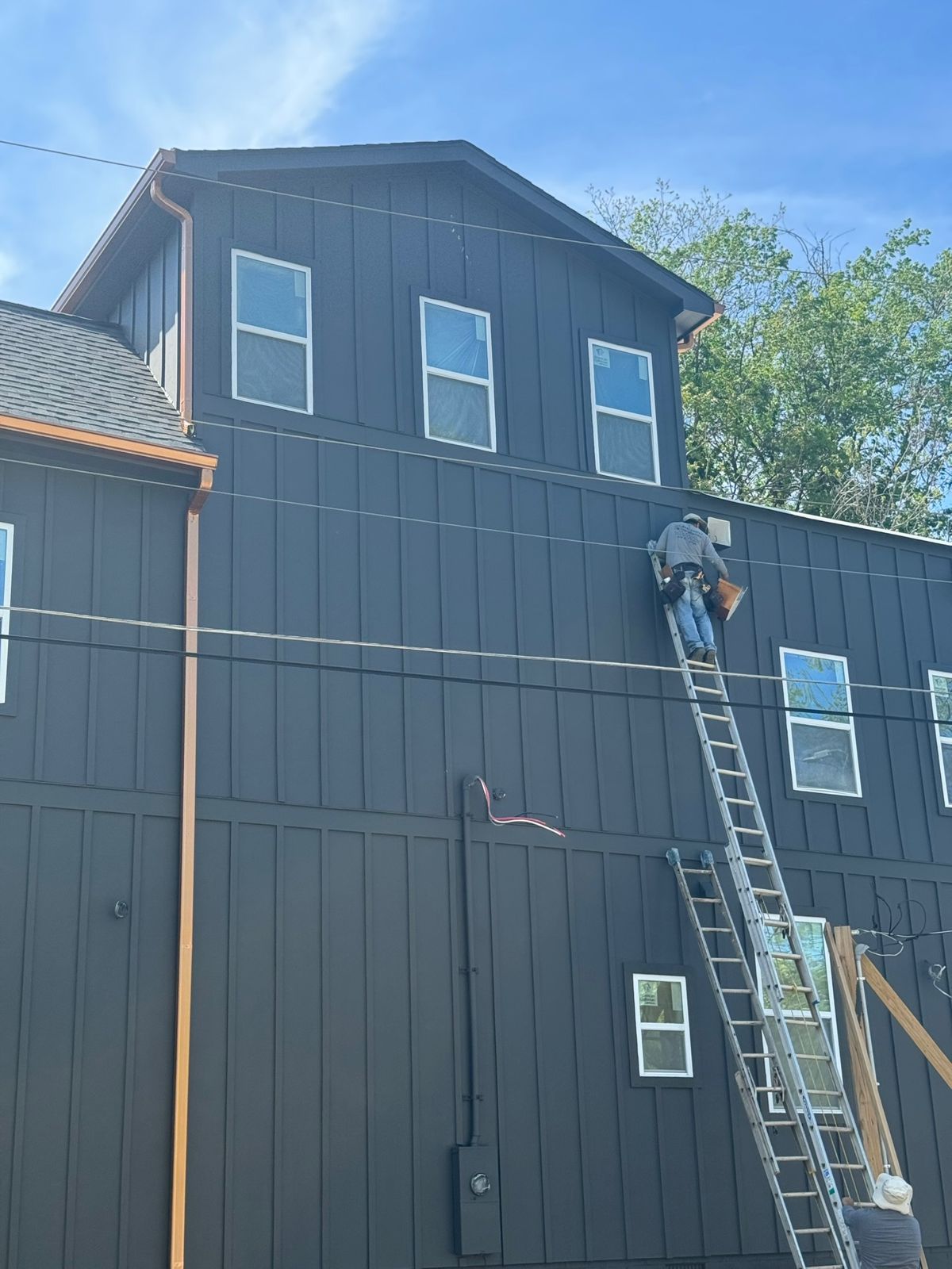 Crew installing dark board-and-batten siding and copper gutters