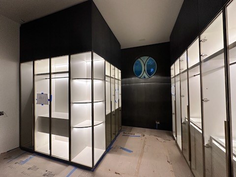 Lit glass wardrobes lining both sides of a walk-in closet