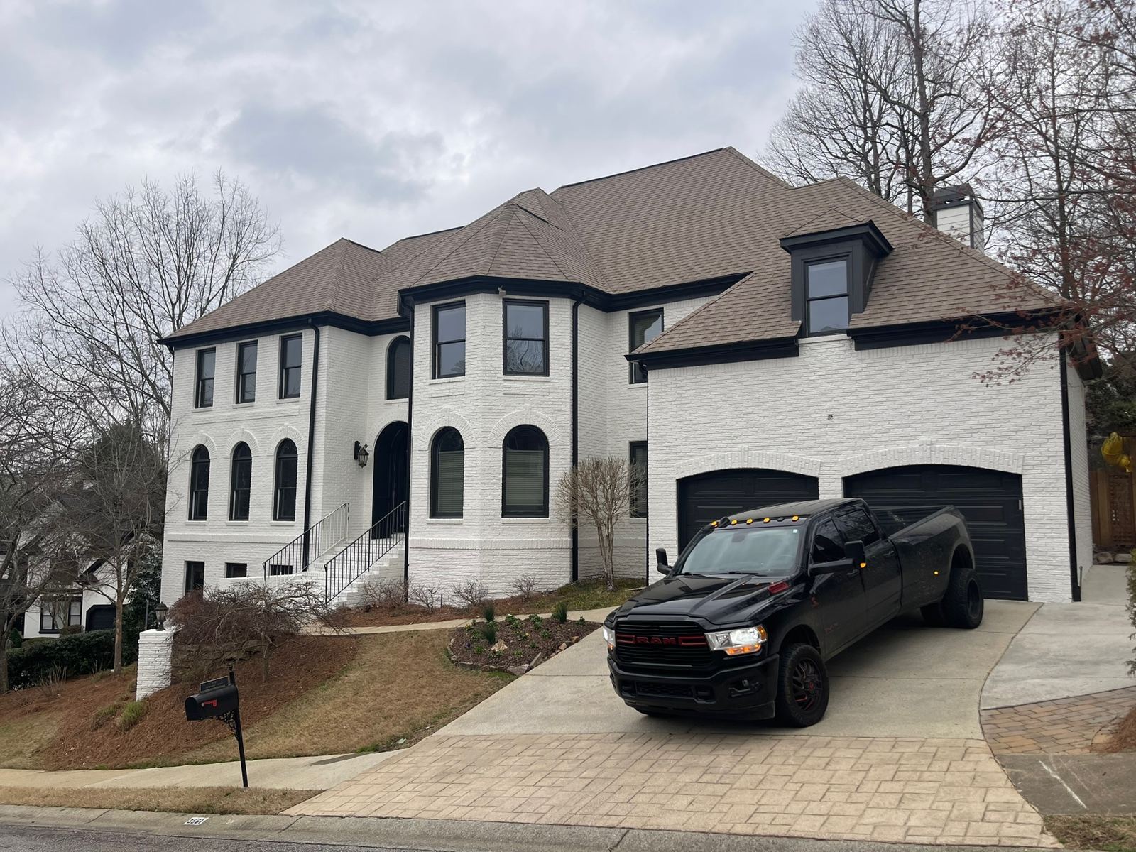 Front of a white brick custom home with turret, arched windows and two-car garage